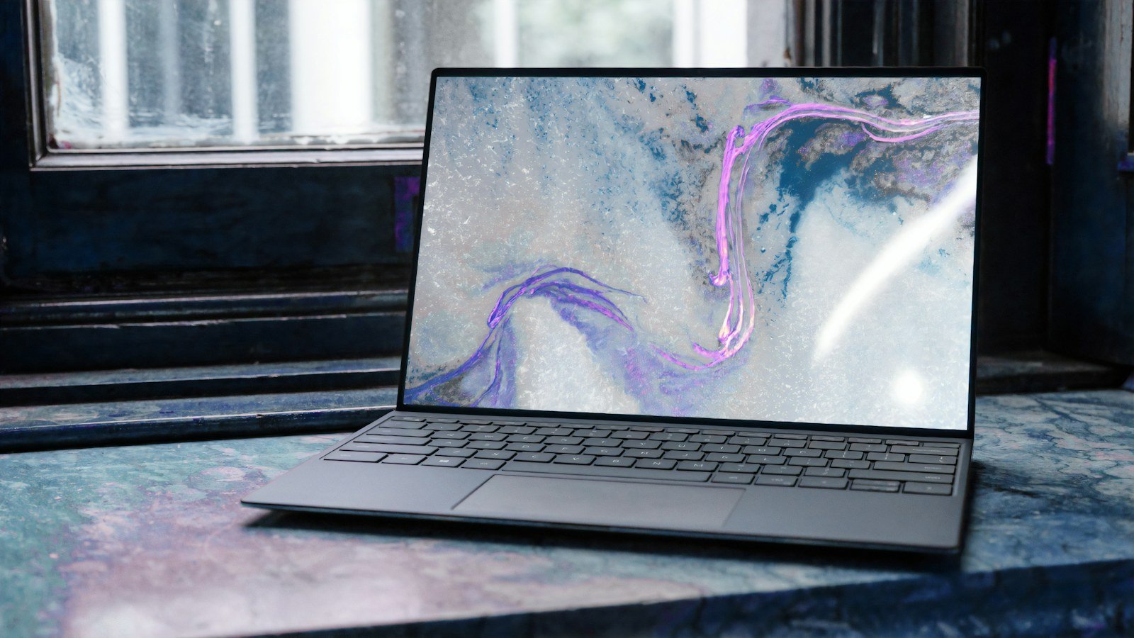Thin laptop open on a marble surface by a window